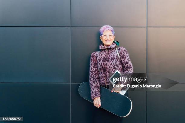 italy, portrait of fashionable senior woman with skateboard and digital tablet - purple hair stockfoto's en -beelden