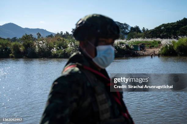General view of the temporary campsite of the internally displaced people from Myanmar is seen behind a Thai soldier who guards the river bank of the...