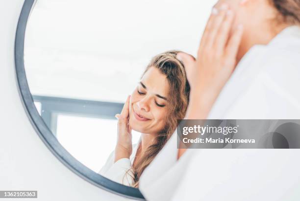 woman enjoys routine applying moisturizing cream on face - applying cream stock pictures, royalty-free photos & images