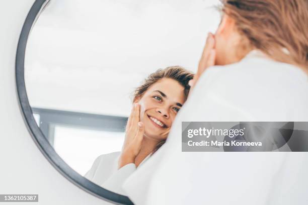 woman enjoys routine applying moisturizing cream on face - lounge chair photos et images de collection