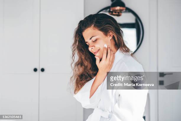 woman enjoys routine applying moisturizing cream on face - untar fotografías e imágenes de stock