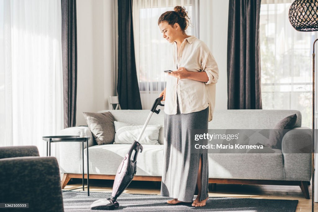 Woman doing house work. Woman talking on cell phone while vacuuming floor.
