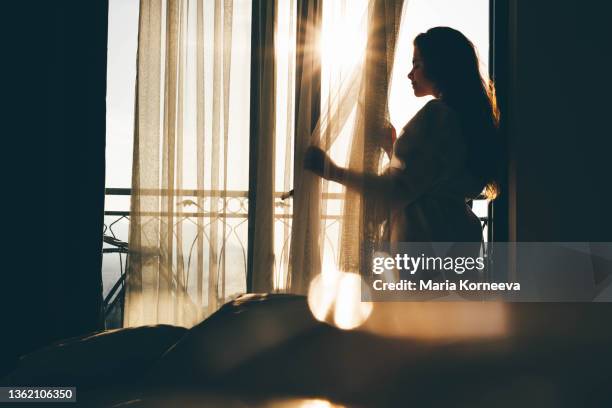 woman in bathrobe opens curtain to enjoy view - curtain hotel stock-fotos und bilder