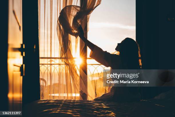 woman opens curtain to enjoy view from big window in morning - bedroom window foto e immagini stock