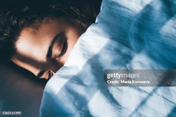 lady sleeps in bed tossing turning in dream under blanket - sleeping foto e immagini stock