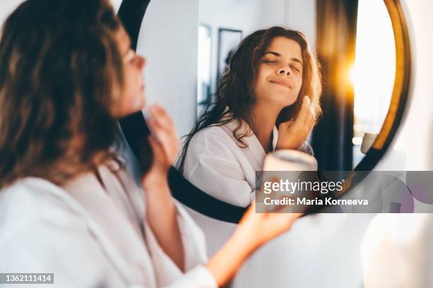 woman enjoys routine applying moisturizing cream on face - applying cream stock pictures, royalty-free photos & images