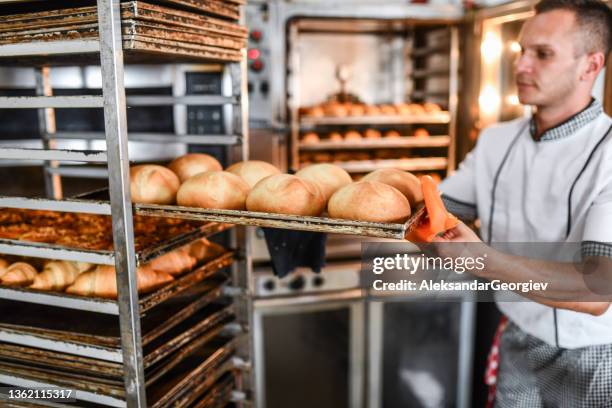 male baker taking fresh bread smelling nicely right out of oven - baker smelling bread stock pictures, royalty-free photos & images