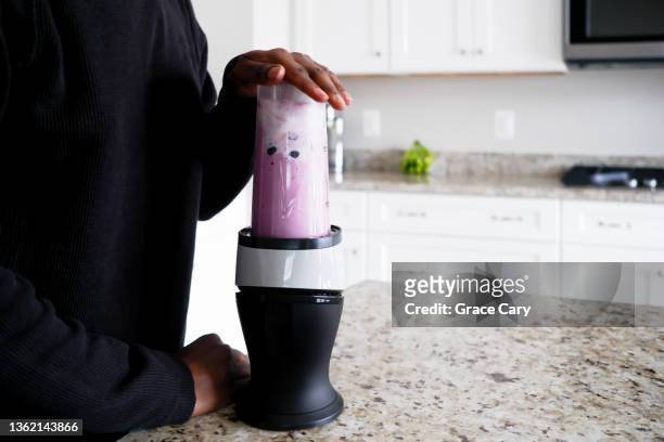 woman makes blueberry banana smoothie - mixer stock-fotos und bilder