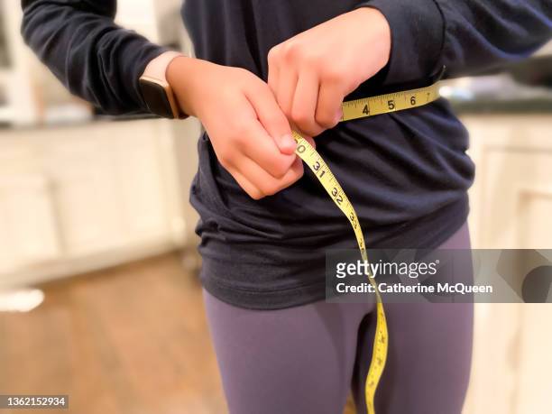mixed-race young female measuring waistline with tape measure - eating disorder stock pictures, royalty-free photos & images