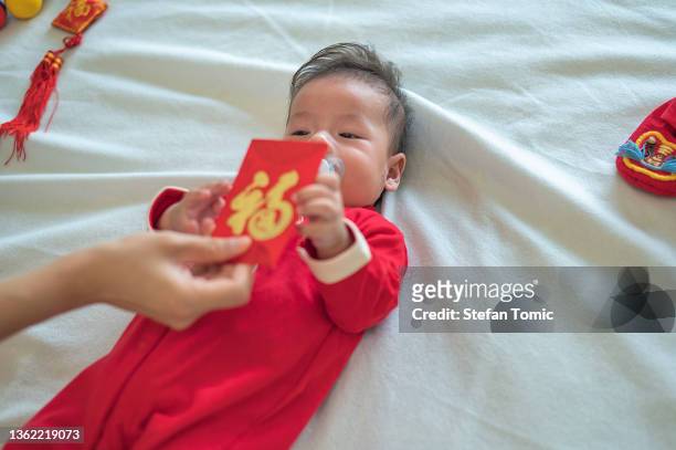 kleiner junge erhält roten taschenumschlag mit traditionellem roten anzug für das mondneujahr - chinese new year red envelope stock-fotos und bilder