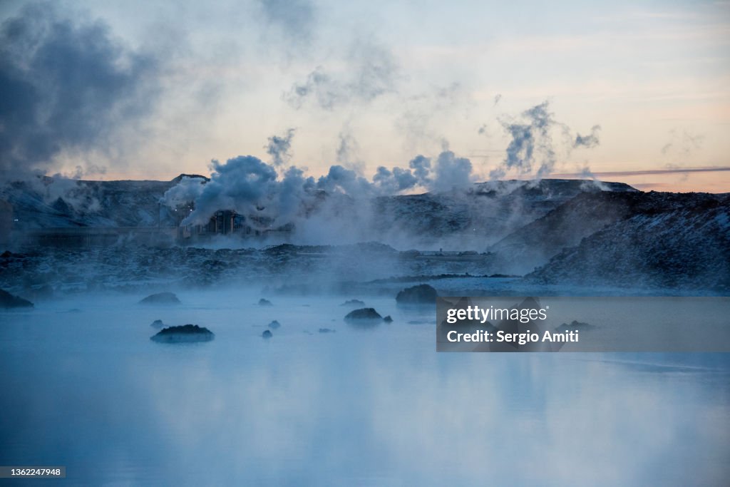 Icelandic geothermal blue hot spring in lava stones covered with snow at sunset