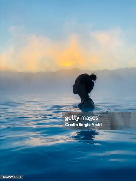 woman bathing in icelandic geothermal blue hot spring at sunset - blue lagoon iceland stock-fotos und bilder