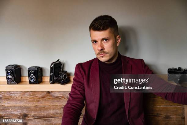 confident caucasian male fashion model posing with an antique analog camera - tache café stockfoto's en -beelden