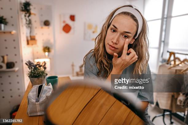 woman rubbing cream under eyes - woman mirror stockfoto's en -beelden
