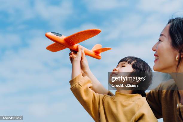 young asian mother and lovely little daughter spending time together outdoors, playing with airplane toy and smiling joyfully in park on a lovely sunny day against beautiful blue sky - school life balance stock pictures, royalty-free photos & images