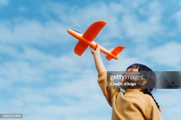 happy lovely little asian girl having fun outdoors, playing with airplane toy and smiling joyfully in park on a lovely sunny day against beautiful blue sky - finding hope stock pictures, royalty-free photos & images