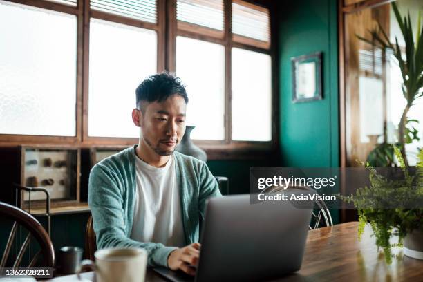 professional young asian man working from home, using laptop computer in home office. remote working, freelancer, small business concept - kantoor thuis stockfoto's en -beelden