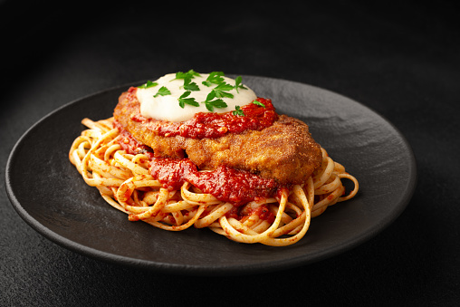 Chicken parmigiano with linguini pasta on a plate black background