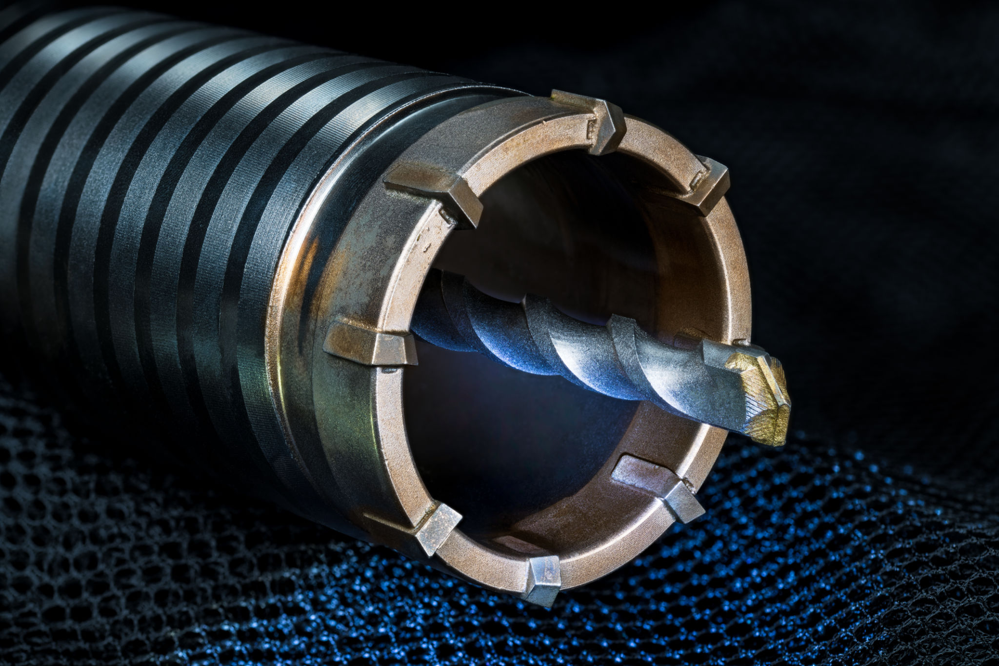 Detail of hole saw cutter of ring shape with spiral pilot drill bit on blue net with a black background Detail of hole saw cutter of ring shape with spiral pilot drill bit on blue net with a black background