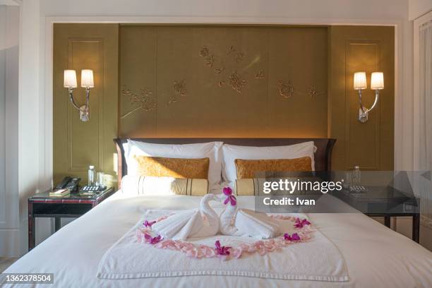 two towel swans kissing each other on the bed, their heads form a heart. rose pedals all around. - hotel suite fotografías e imágenes de stock