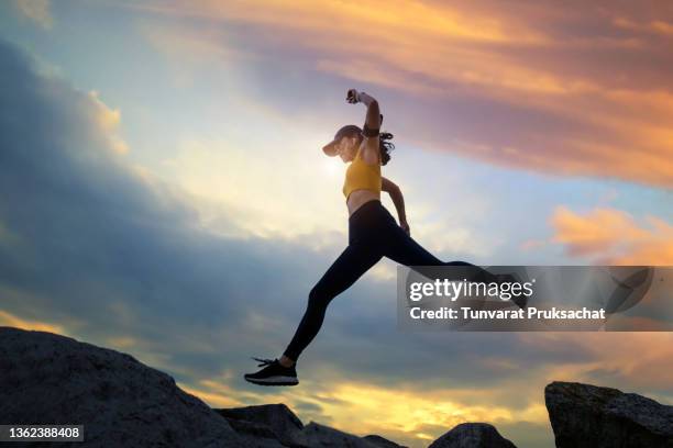 asian woman runs and jumping on mountain ridge at sunset. - forward athlete foto e immagini stock
