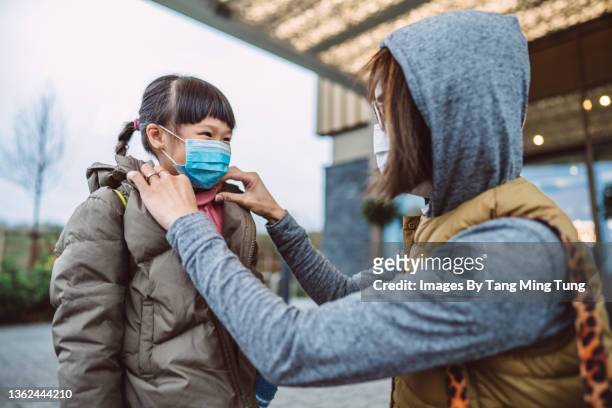 mom helping her daughter to wear medical face mask outside a hotel building - coronavirus winter stock-fotos und bilder