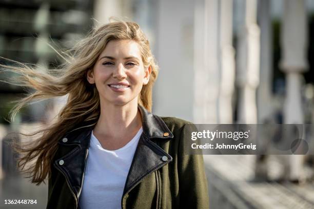 portrait of carefree early 30s woman walking in sunshine - wit jak stockfoto's en -beelden