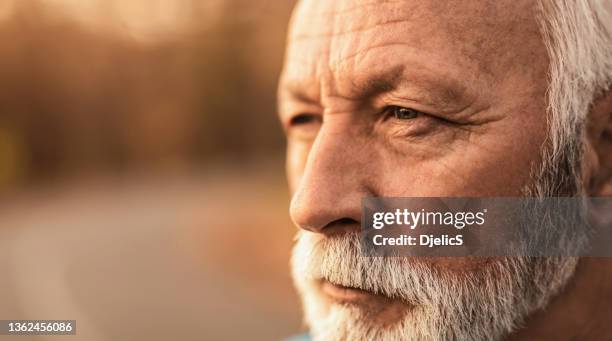 stellen sie sich einer nahaufnahme eines ernsthaften älteren mannes gegenüber, der den sonnenuntergang betrachtet und nachdenkt. - männer portrait gesicht close up stock-fotos und bilder