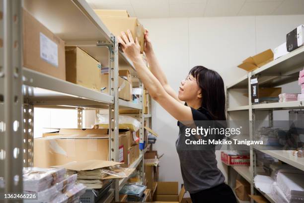 woman taking a box down from the shelf in her office - transparent box stock pictures, royalty-free photos & images