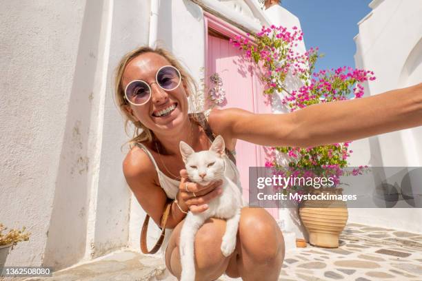 young woman takes a selfie in a cute little village with a white cat - undomesticated cat stockfoto's en -beelden