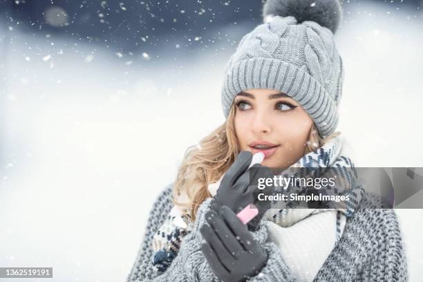 gorgeous blonde puts on lip balm dressed in woolen clothes outdoors on a cold winter day. - lip balm stock pictures, royalty-free photos & images