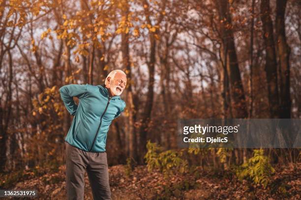 senior sportsman having a backache while exercising in nature. - bending over stock pictures, royalty-free photos & images