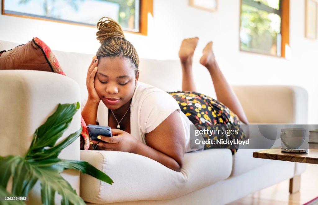 African woman relaxing on sofa with her mobile phone