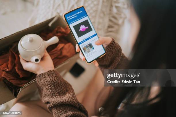 unhappy asian chinese woman complaining using mobile app on received different colour teapot from online shopping a living room - newly opened stock pictures, royalty-free photos & images