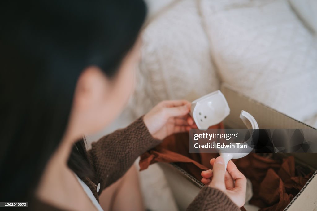 Unhappy asian chinese woman holding broken ceramic teapot from online shopping a living room