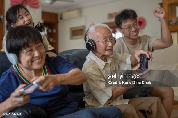 2 asiatische chinesische großeltern spielen videospiel zu hause mit enkelkindern. - chinese family taking photo at home stock-fotos und bilder