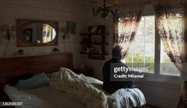 lonely senior man looking out of window at bedroom - un solo hombre mayor fotografías e imágenes de stock