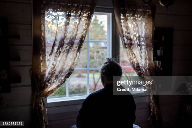 lonely senior man looking out of window - depressione foto e immagini stock