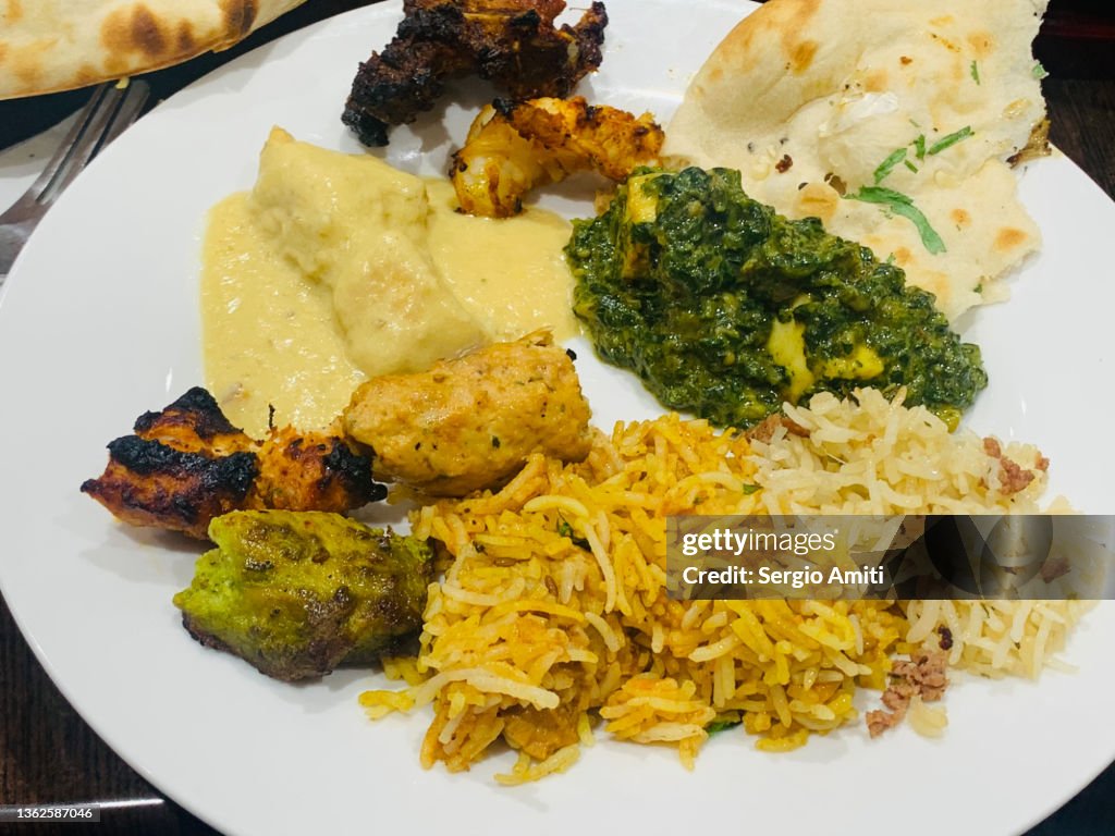 Plate with Indian tandoori mixed platter, lamb biryani, malai chicken korma, Saad paneer and garlic naan bread