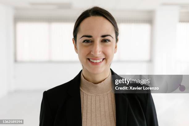 real estate woman agent looking at camera and smiling while standing in an empty office. - empleada administrativa stock pictures, royalty-free photos & images