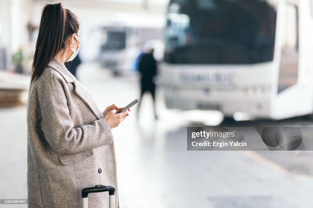 Mujer joven sosteniendo un teléfono inteligente mientras espera el autobús