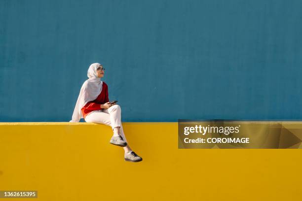 young arab woman using her mobile phone while listening to music with headphones outdoors. - arab lifestyle stockfoto's en -beelden