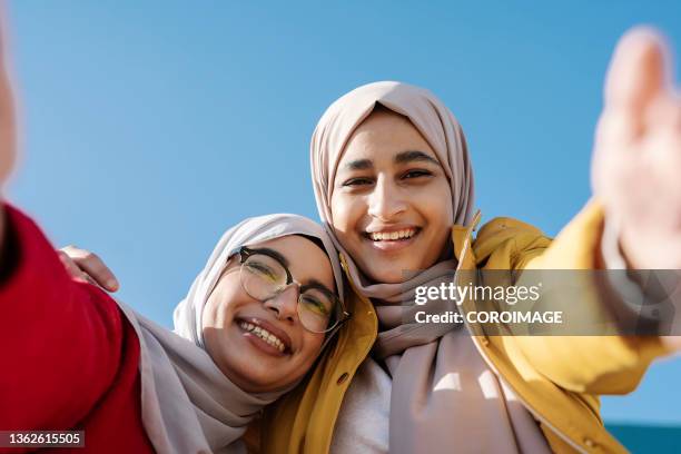 young arab female friends smiling while taking a selfie together outdoors. - selfie stock pictures, royalty-free photos & images