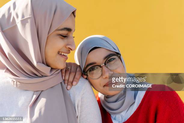 two young arab women smiling while posing together outdoors against a yellow wall. yellow background. - beautiful arabian girls stock pictures, royalty-free photos & images