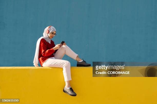 young muslim woman enjoying listening to music with a smartphone and headphones outdoors. - islam stock-fotos und bilder