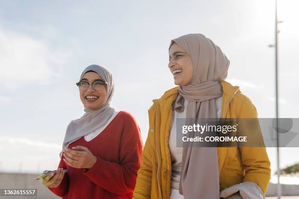 two arab female friends smiling and having fun while walking down the street together. - arab woman walking stock-fotos und bilder
