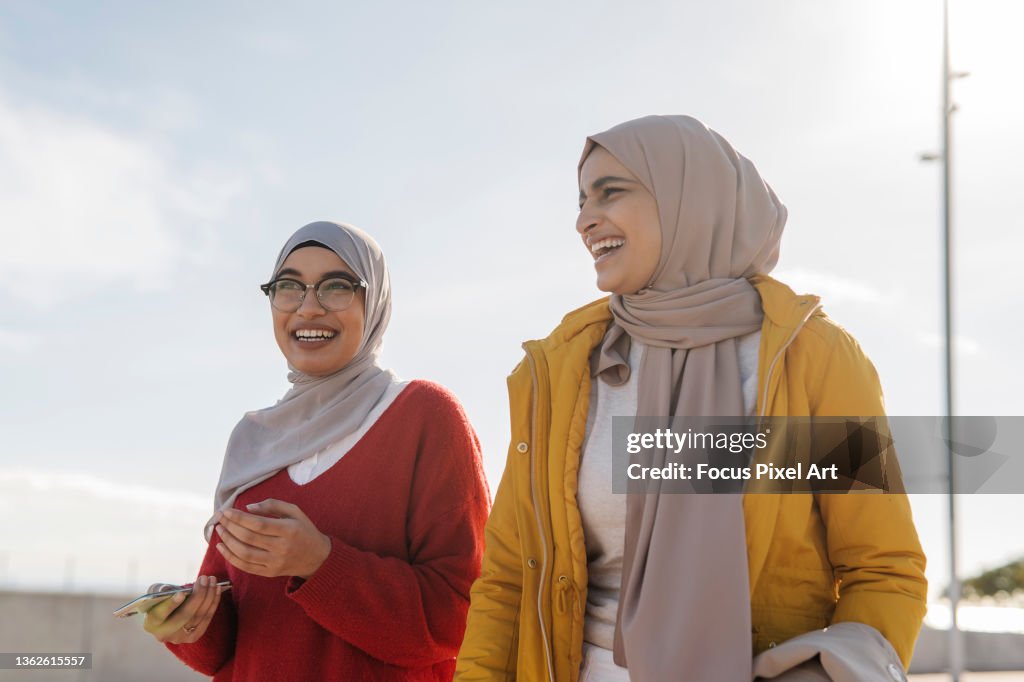Two Arab female friends smiling and having fun while walking down the street together.