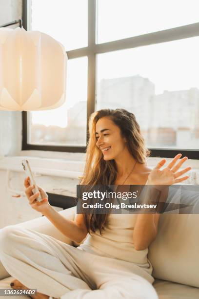 cheerful woman having video call with friends on smartphone. waves her hand to say hello, live broadcast - friends laughing at iphone video stock pictures, royalty-free photos & images