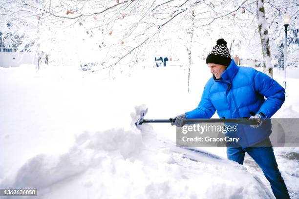 man shovels snow from car in driveway after winter storm - shoveling snow stock pictures, royalty-free photos & images