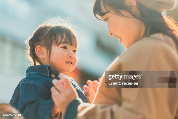 madre y niña pequeña sentadas en el banco y disfrutando de pasar tiempo juntas en la ciudad en invierno en un día soleado y cálido - familia de dos generaciones fotografías e imágenes de stock